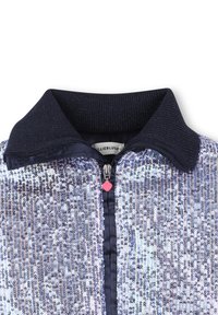 Navyblaue Jacke mit geripptem Kragen und Frontreißverschluss, bedeckt mit silbernen Pailletten, herzförmiger pinker Reißverschlussanhänger sichtbar.