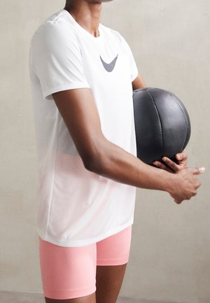 Witte sportieve shirt met een grijs logo, gecombineerd met roze shorts. Persoon houdt een zwarte medicinal bal vast, die een gladde, ronde textuur toont.