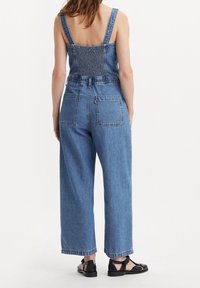 Jeansbyxor med vida ben, ljusblå färg, smockad ryggdetalj och två bakfickor. Justerbara axelband och rå kant.