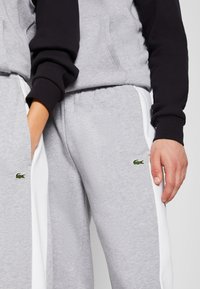 Grijze katoen sweatpants met witte zijstrepen en een klein groen geborduurd logo. Gladde textuur met een elastische tailleband en zakken.