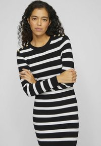 Svart- och vitrandig tröjdress med långa ärmar, ribbad textur och gyllene knappdetaljer på axlarna. Åtsittande design.