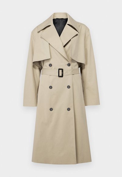 Beige trench coat dengan desain double-breasted, kerah besar, pinggang berikat, dan detail flap di bahu. Kain tampak halus.