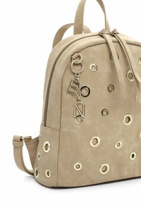 Zaino beige in suede con dettagli in occhielli dorati e un ciondolo decorativo. Dispone di chiusura con zip e spallacci regolabili per il massimo comfort.