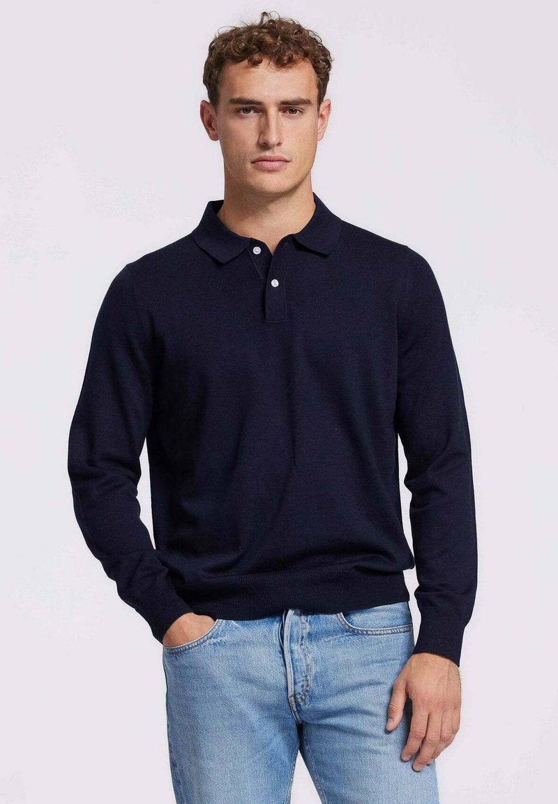 Marineblauwe longsleeve polo met een kraag, een twee-knopen sluiting en geribbelde manchetten, gecombineerd met lichtblauwe denim jeans.