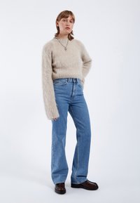 Beige fluffig tröja med långa ärmar ihop med högmidjade blå jeans och mörkbruna plattformsskor. En enkel, mjuk och avslappnad look.