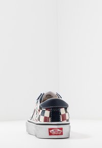 Vans sneaker rendah dengan pola kotak-kotak merah, putih, dan biru, tumit navy, dan logo "Vans Off The Wall" merah pada sol putih.