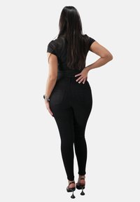 Czarne dopasowane dżinsy z wysokim stanem i subtelnymi tylnymi kieszeniami, w połączeniu z czarną bluzką i sandałami na wysokim obcasie, widok z tyłu.