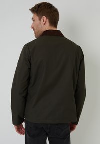 Veste vert foncé en tissu lisse avec un col en velours côtelé marron. Présente une coupe décontractée et des détails minimalistes. Vue de dos.