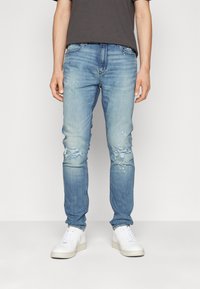 Jasnoniebieskie dżinsy z przetarciami i plamami farby. Slim fit z standardowym pasem i kieszeniami z przodu.