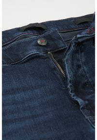 Mørkeblå denimjeans med en glat tekstur, der har en metalknap, lynlås lukning og kontrasterende rød syning langs taljen.