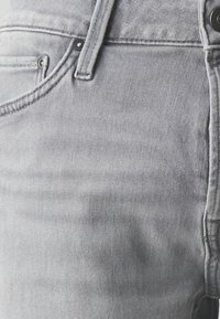 Vaqueros de mezclilla gris con un acabado texturizado, diseño clásico de cinco bolsillos y herrajes metálicos en el botón y remaches.