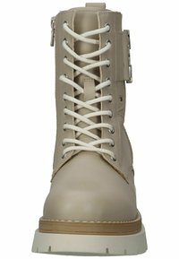 Botín de cuero beige hasta el tobillo con cordones blancos, cremallera lateral y suela de goma clara. Presenta detalles de costura y acentos metálicos.