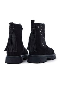 Botas de ante negras hasta el tobillo con suela gruesa, con borlas decorativas y acentos metálicos en forma de estrella en el costado. Cierre de cremallera en la parte trasera.