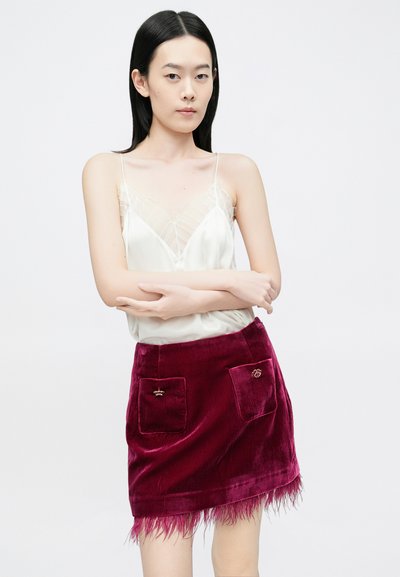 Kreemjas satiinist kampsun õhukeste detailidega, sobitatud bordoopunase sametise miniseeliku juurde, millel on ees kaks taskut ja sulgedega ääristus.