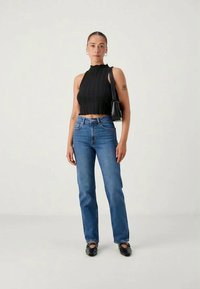Black ribbed crop top with a round neckline, paired with blue straight-leg jeans and black slip-on shoes. Minimalist handbag accent.