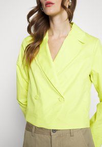 Lime green double-breasted jacket with notched collar, made of lightweight fabric. Features smooth texture and two button closures.