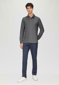 Langarm-Polo aus dunkelgrauem Stoff mit einem knöpfbaren Kragen, kombiniert mit marineblauen Hosen und weißen Turnschuhen, vor einem neutralen Hintergrund präsentiert.