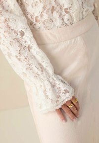 Lace blouse with floral pattern featuring puffed sleeves, paired with a light pink, smooth-textured skirt, showcasing layered fabric details.