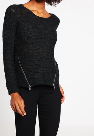 Maglione nero lavorato a maglia con maniche lunghe, caratterizzato da un collo rotondo e dettagli con zip argentate ai lati. Materiale testurizzato e design aderente.