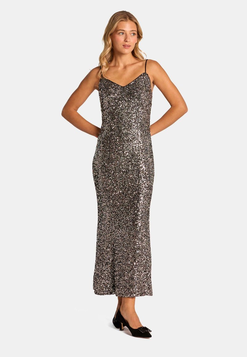 Sukienka wieczorowa ozdobiona cekinami ma dopasowany krój, dekolt w kształcie litery V oraz cienkie ramiączka. Kolory przeważająco srebrny i czarny, z błyszczącą teksturą.