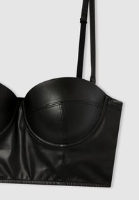 Reggiseno senza spalline in pelle nera con coppe sagomate, una superficie liscia e un design strutturato con dettagli delle cuciture. Inclusi spallacci neri regolabili.