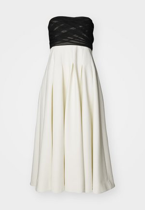 Stropeløs kjole med et sort tekstureret bodice og en hvid plisseret nederdel. Har glat stof, struktureret form og knælangt design.