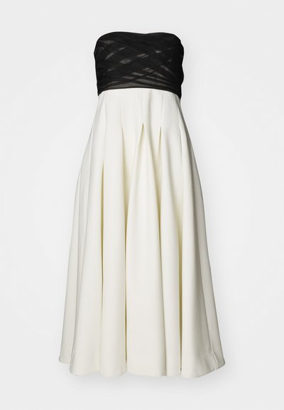 Φόρεμα χωρίς τιράντες με μαύρη υφή στον κορμό και άσπρη πλισέ φούστα. Εχει λείο ύφασμα, δομημένο σχήμα και μήκος μέχρι το γόνατο.