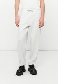 Pantalones de chándal gris claro con cintura elástica y cordón ajustable. La tela es suave con una textura lisa, combinados con zapatos negros.