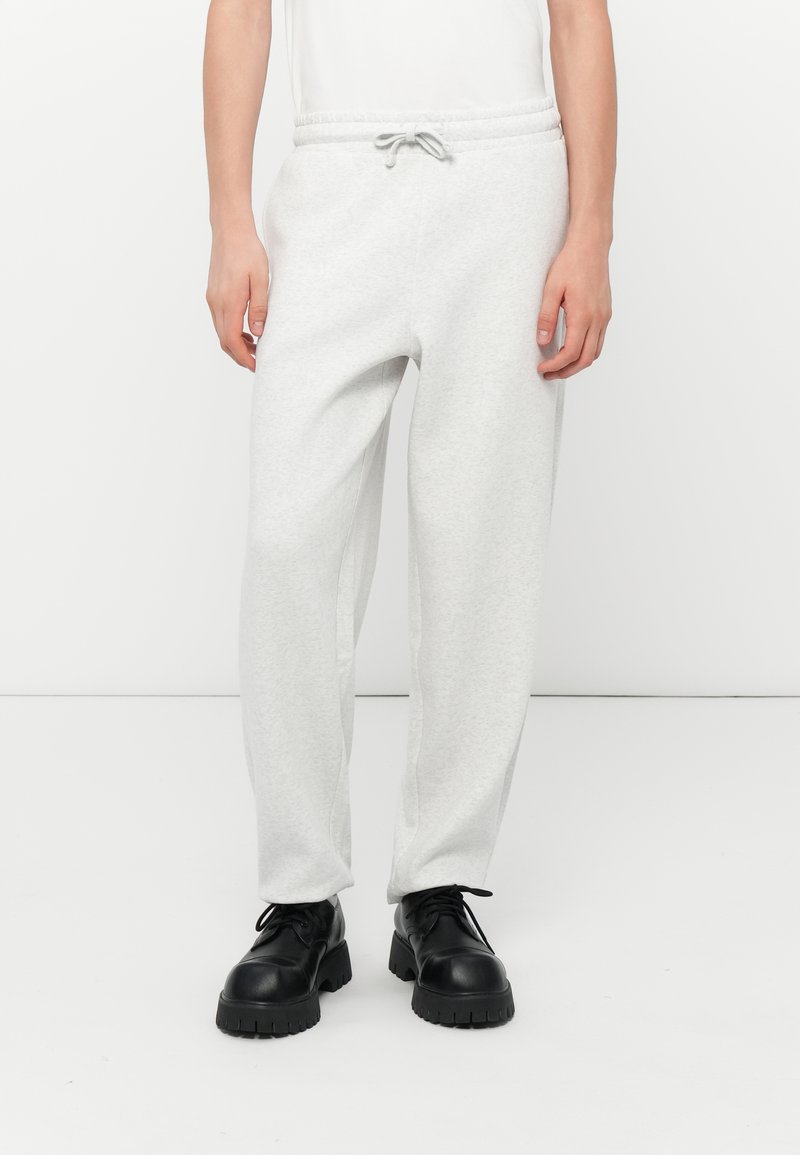 Pantalones de chándal gris claro con cintura elástica y cordón ajustable. La tela es suave con una textura lisa, combinados con zapatos negros.