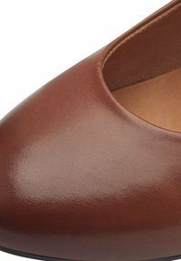Chaussure en cuir marron avec un bout pointu et un design ajouré, présentant une texture lisse et un intérieur doux. Silhouette simple et élégante.