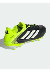 Zwarte en neongele voetbalschoenen met drie witte strepen, een gestructureerde bovenkant en een gemoldzool met gele noppen. "COPA" merk zichtbaar.