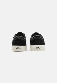 Black suede low-top sneakers with white rubber soles. Accented with white stitching and embossed logo detail on the heel.