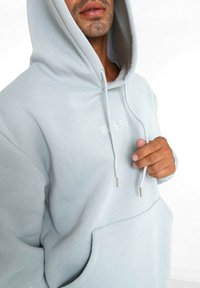 Felpa con cappuccio azzurro chiaro realizzata in tessuto morbido, con tasca frontale, stringhe con punte metalliche e testo ricamato.