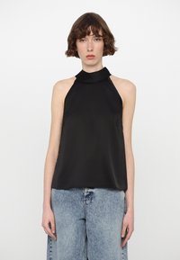 Melnā halter top blūze no gludas, vieglas auduma ar augstu apkakli un atvērtām plecu daļām, apvienota ar gaiši ziliem platmalu džinsiem.
