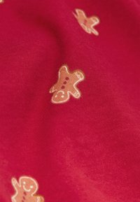 Červená látka s opakujícím se vzorem perníčků v světle hnědé barvě, s detaily jako knoflíky zobrazenými tmavším odstínem.