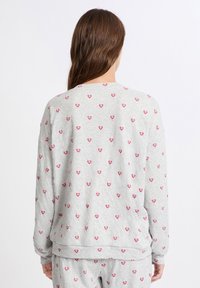 Top gris de manga larga con un pequeño patrón de corazones rosas, hecho de tela suave. Presenta un escote redondeado y puños acanalados.