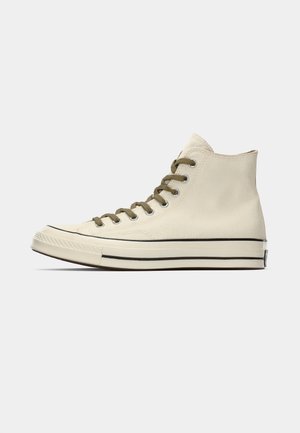 Beige Canvas High-Top-Sneaker mit olivgrünen Schnürsenkeln und schwarz gestreifter Sohle. Minimalistisches Design mit klassischer Silhouette.