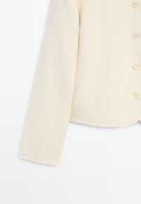 Langsleeve van een crèmekleurige wollen cardigan met bijpassende crèmekleurige knopen op een witte achtergrond.