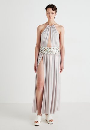 Light gray halter neck dress with keyhole opening, pleated fabric, high slit, and a decorative beaded waistband. Paired with white platform shoes.