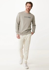 Felpa grigia chiara con un logo testurizzato, abbinata a pantaloni della tuta crema e sneakers bianche. Tessuto morbido e design dalla vestibilità rilassata.