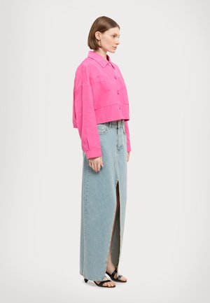 Veste courte rose vif avec fermeture à bouton, associée à une jupe maxi en denim bleu clair dotée d'une fente haute et à des sandales noires.