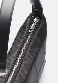 Svart kviltad väska tillverkad av mjukt nylon, med en silverdragkedja och en stilren dragring, kompletterad med ett handtag i svart läder.