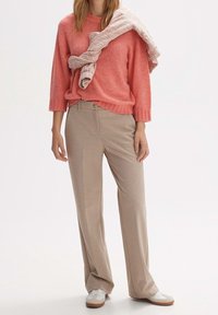Pull en mélange de laine rose à coupe décontractée, associé à un pantalon beige à jambes larges. Baskets blanches avec des accents marron clair.