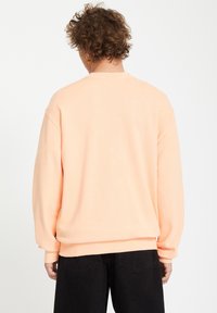Sweatshirt surdimensionné de couleur pêche avec des manches longues et des poignets côtelés, doté d'un col rond et d'un tissu doux et texturé.