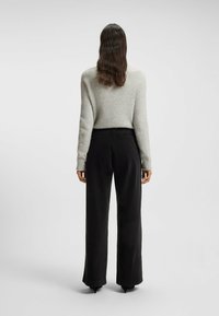 Lichtgrijze, fuzzy trui met een ronde hals, gecombineerd met hoge taille, zwarte wijde pantalon, beide vanuit de rug gezien.