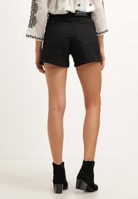 Shorts en denim noir au design ajusté, dotés d'une taille haute, de poches arrière et d'un ourlet retroussé. Assortis à des bottines noires.