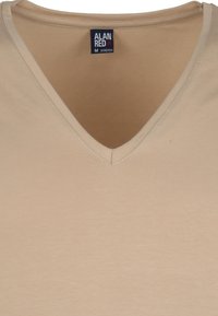 Beige v-hals t-shirt van rekbare stof, met een gladde textuur en subtiele stikdetails. Etiket toont "ALAN RED", maat M.
