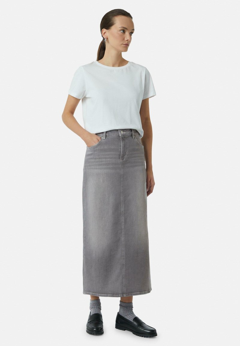 Jupe maxi en denim gris avec taille haute, poches avant et coupe droite. Associée à un t-shirt à col rond blanc et des mocassins noirs.