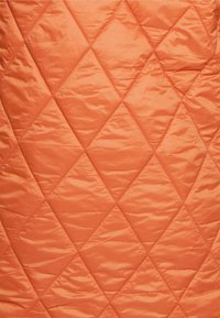 Tessuto arancione trapuntato con un motivo a diamante e una texture liscia e lucida. Le cuciture create formano un design geometrico.