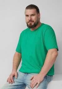 Zielona bawełniana koszulka z krótkim rękawem i okrągłym dekoltem, w połączeniu z jasnoniebieskimi dżinsami. Tkanina ma subtelną teksturę.